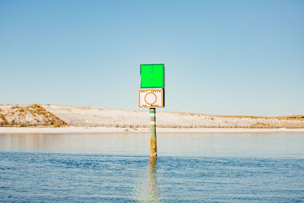 A channel marker standing in shallow turquoise water off a white sand spit
